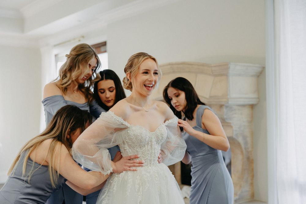 Wedding preparation scene with bridesmaids in gray dresses helping with the bridal gown.