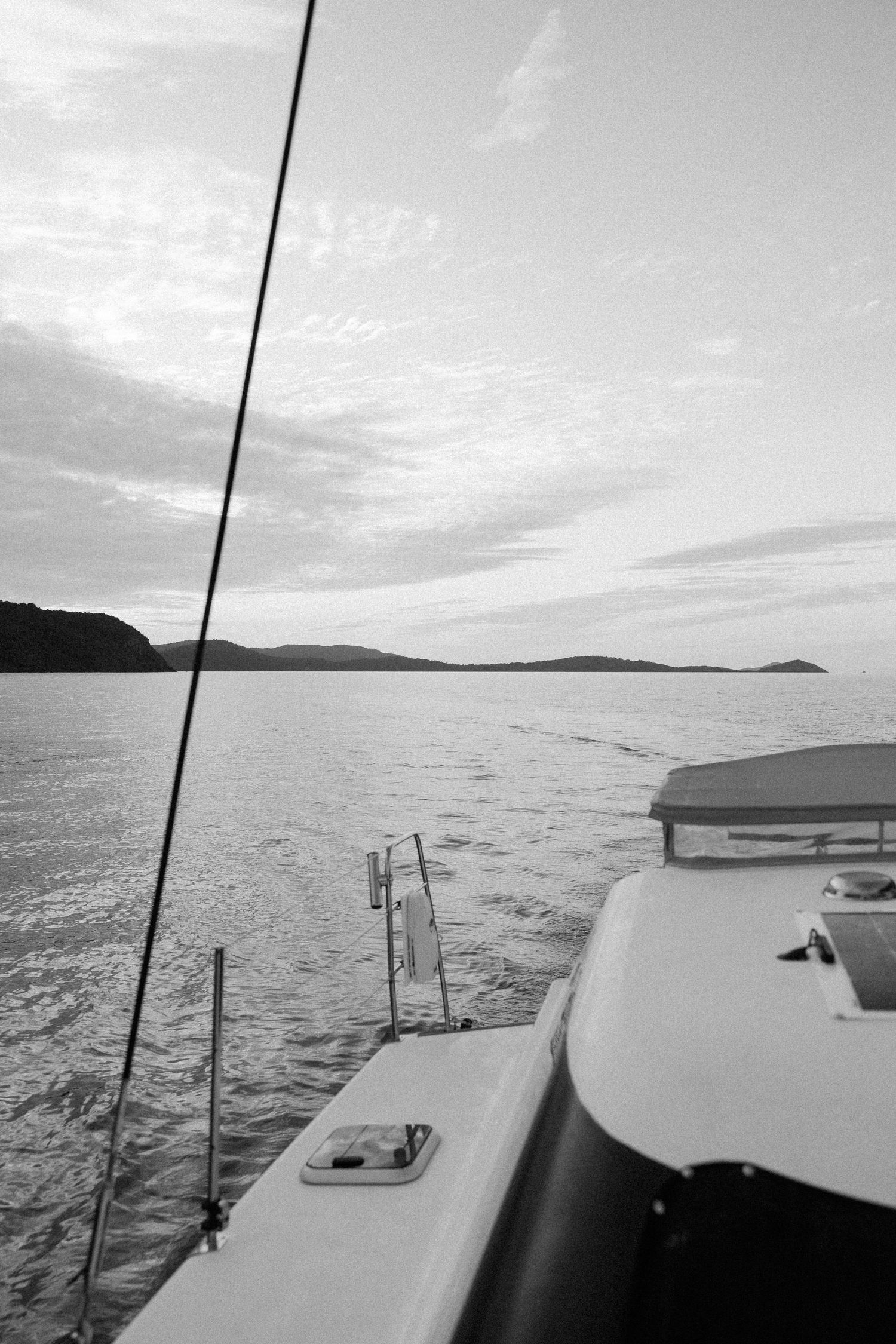 Black and white view from boat deck showing distant hills and water at sunset.
