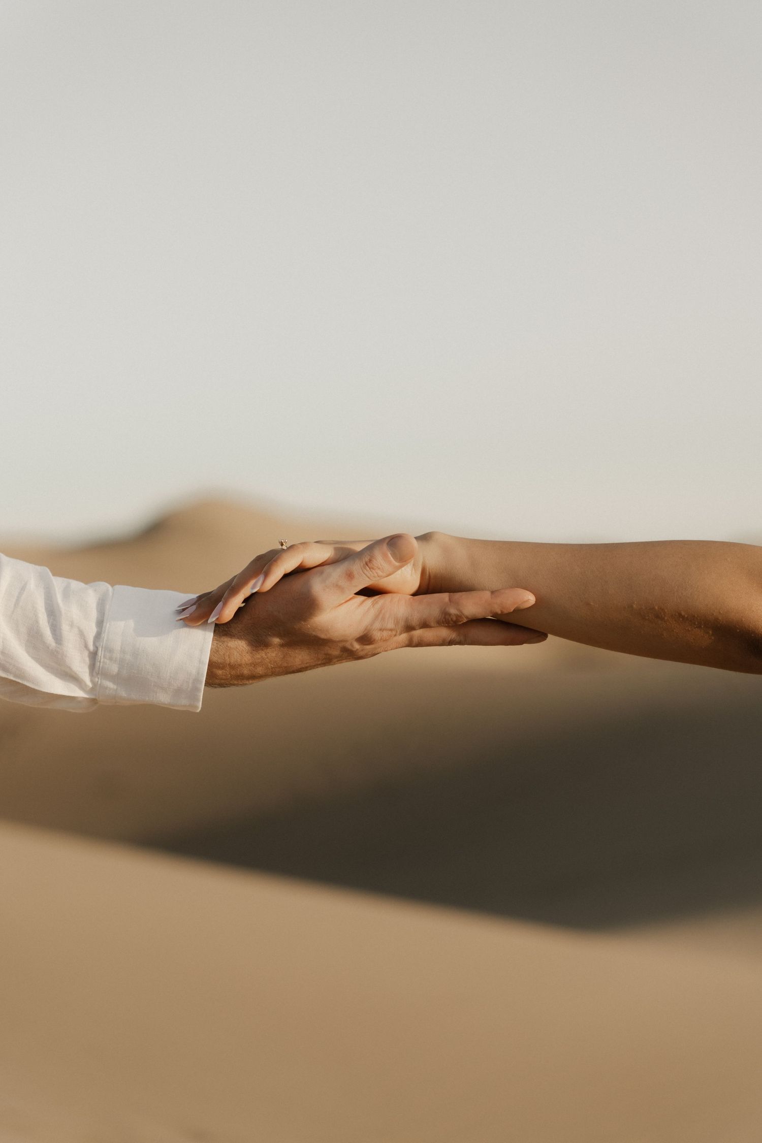 Detail shot of a couple holding hands with sand blowing gently around their feet.