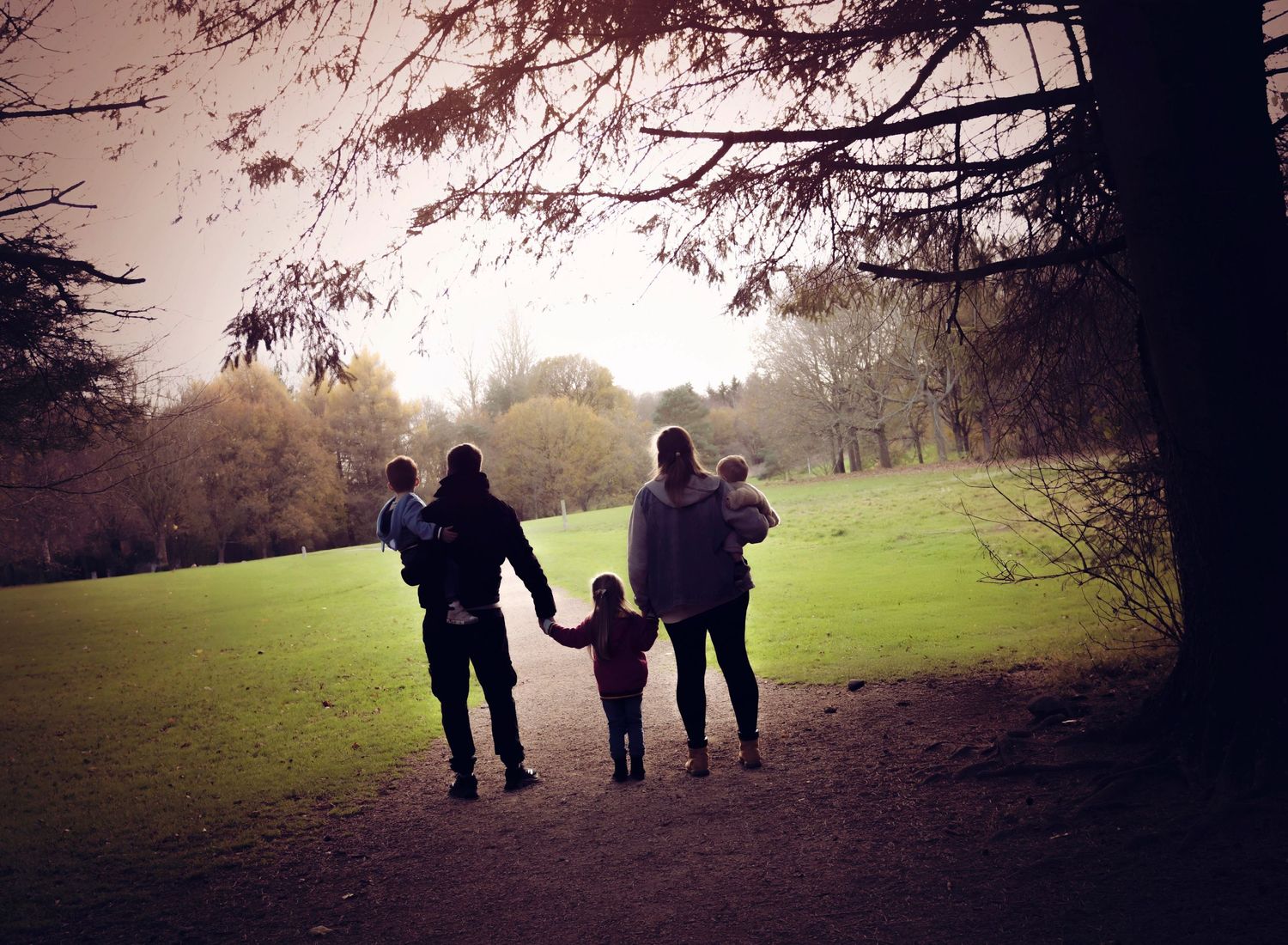 Family outdoor Autumn session at Barlbirnie park. The image is silhouetted under a canopy of trees and the family look away from the camera.
