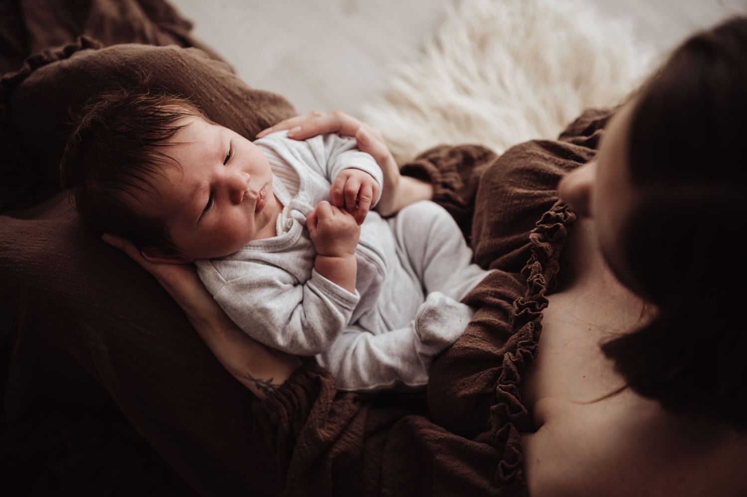 A small child lies cozily on brown blankets while holding a pacifier in a warm, dimly lit setting.