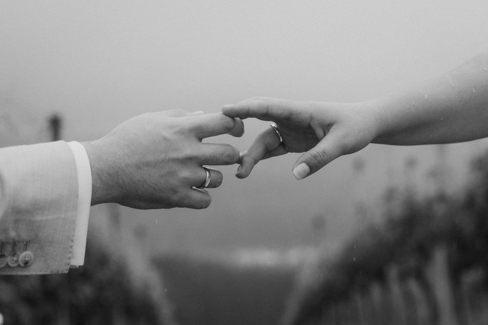 Black and white photo of two hands gently touching, with wedding rings visible, symbolizing love and marriage.