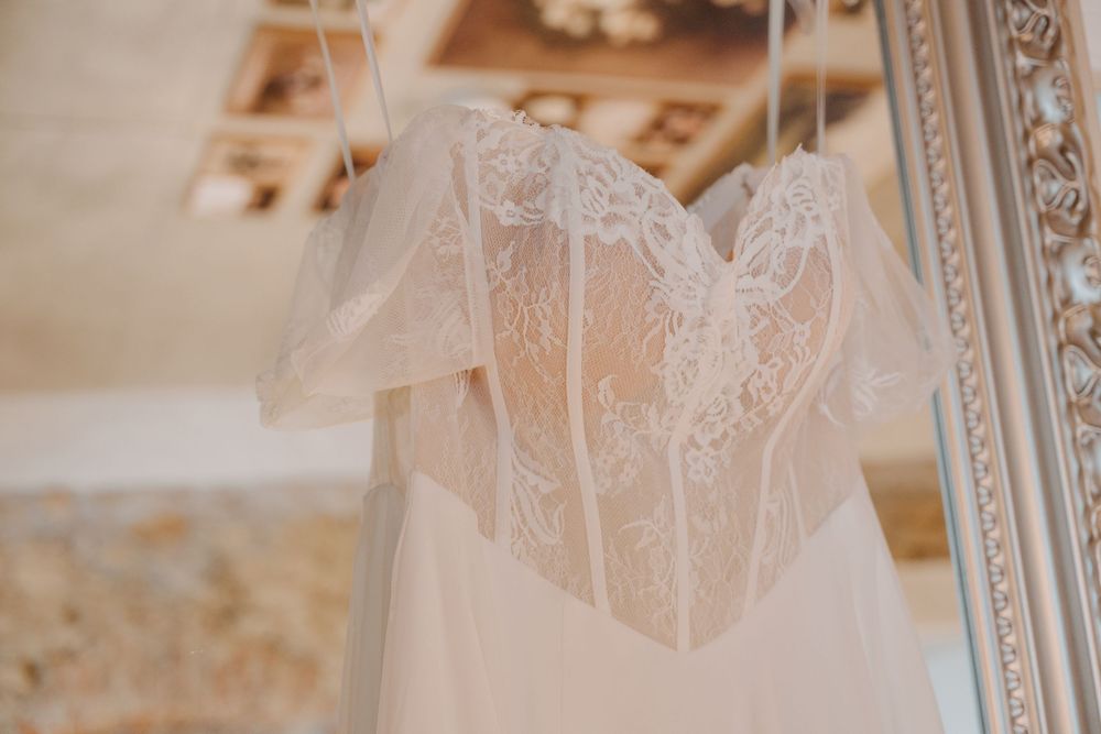 Elegant lace wedding dress with sweetheart neckline and sheer bodice hanging on a decorative mirror frame.