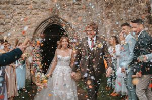 Newlyweds exit stone church amid shower of confetti and flower petals.