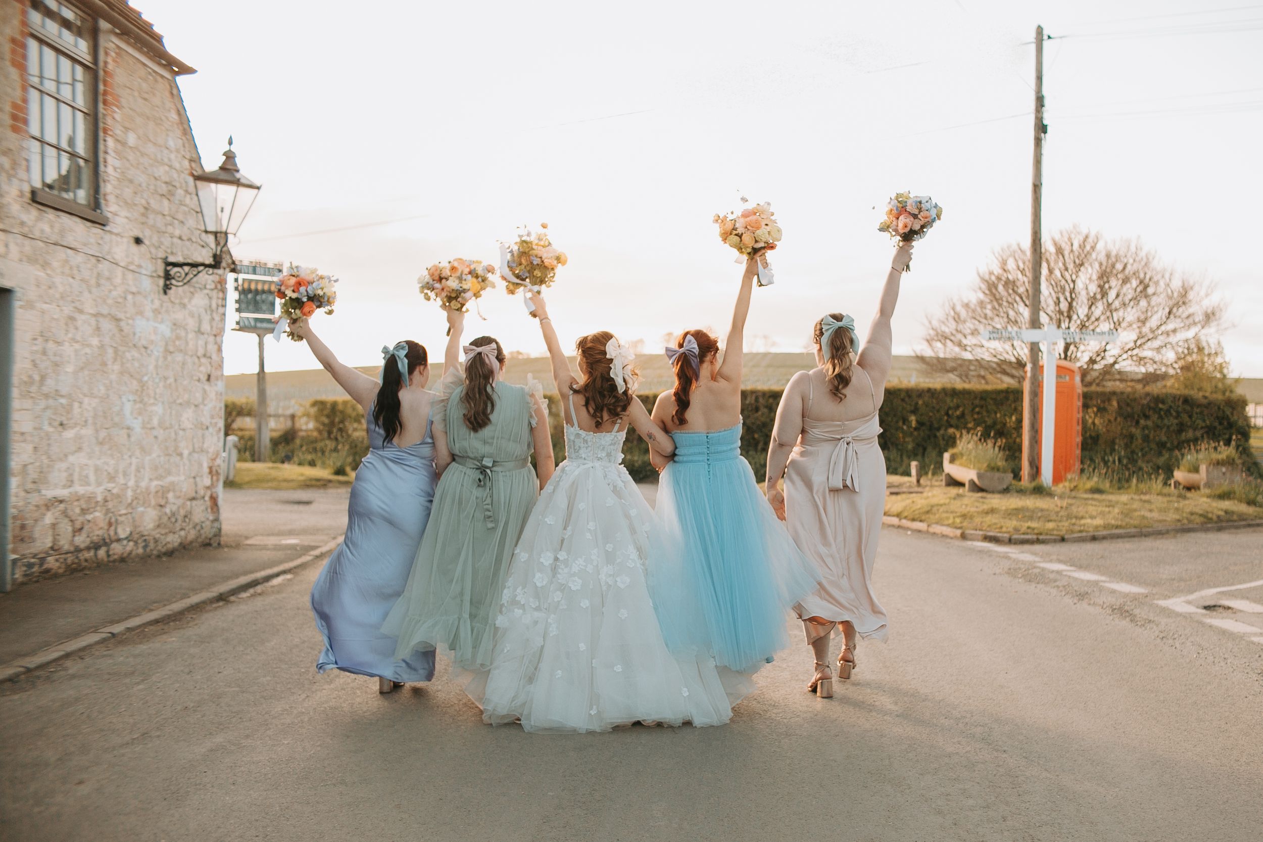 Wedding party celebrates outdoors in flowing pastel gowns with bouquets.