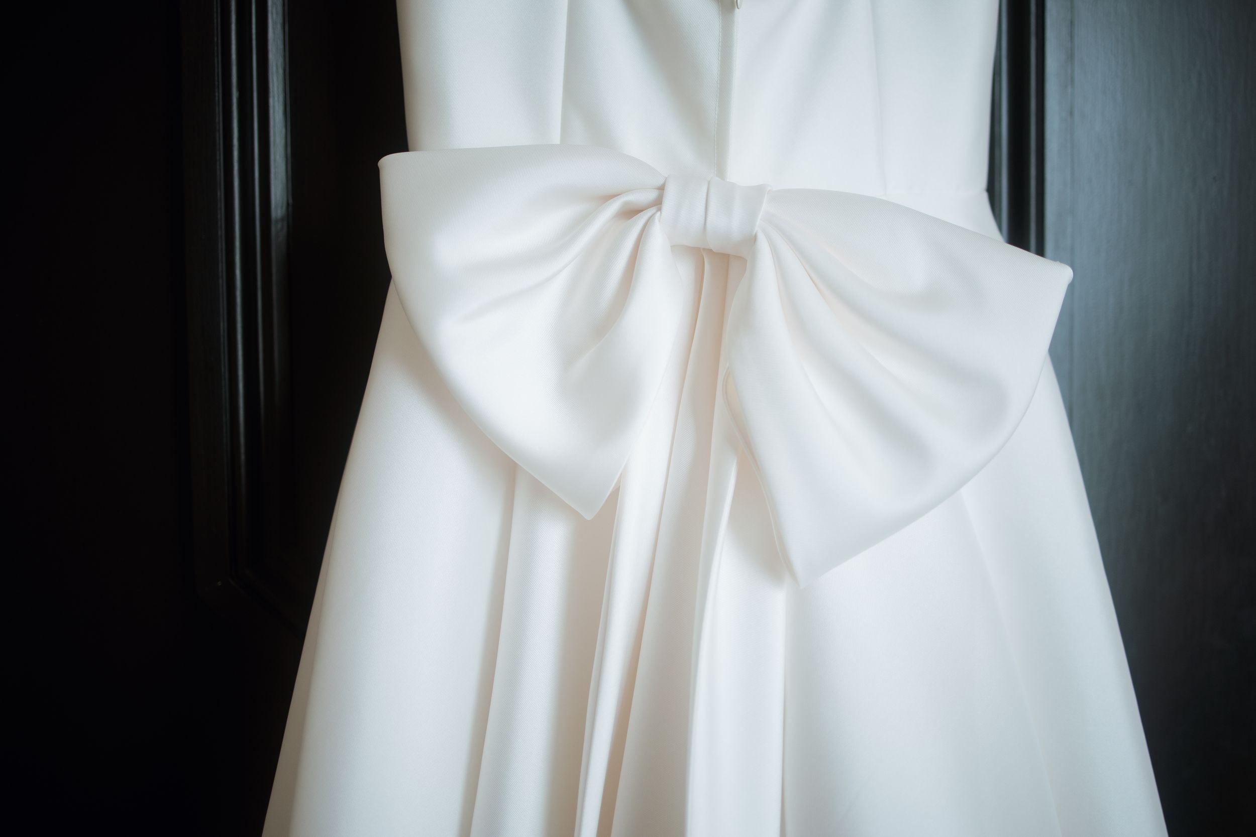 Close-up detail of a white wedding dress bow against a dark background.
