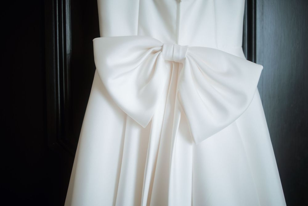 Close-up detail of a white wedding dress bow against a dark background.