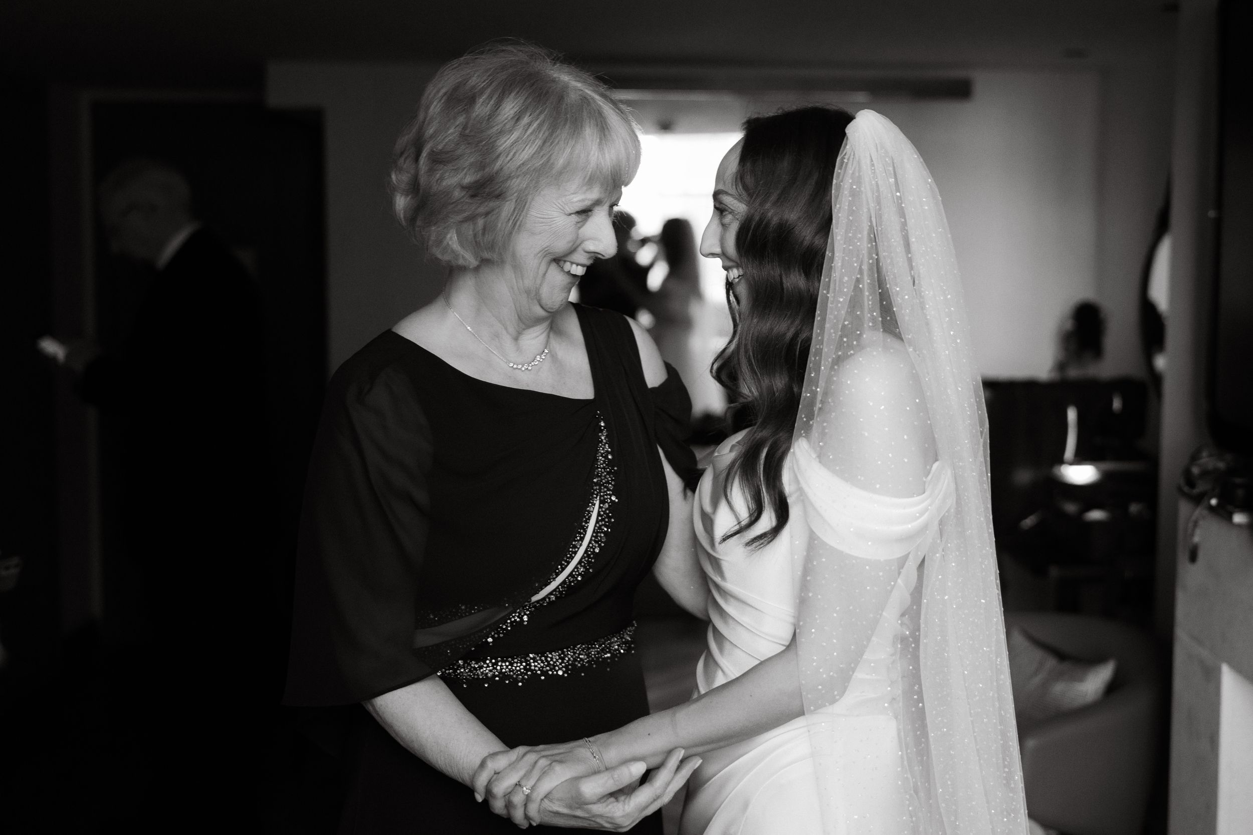 A tender black and white moment between a bride and woman in black during wedding preparations.