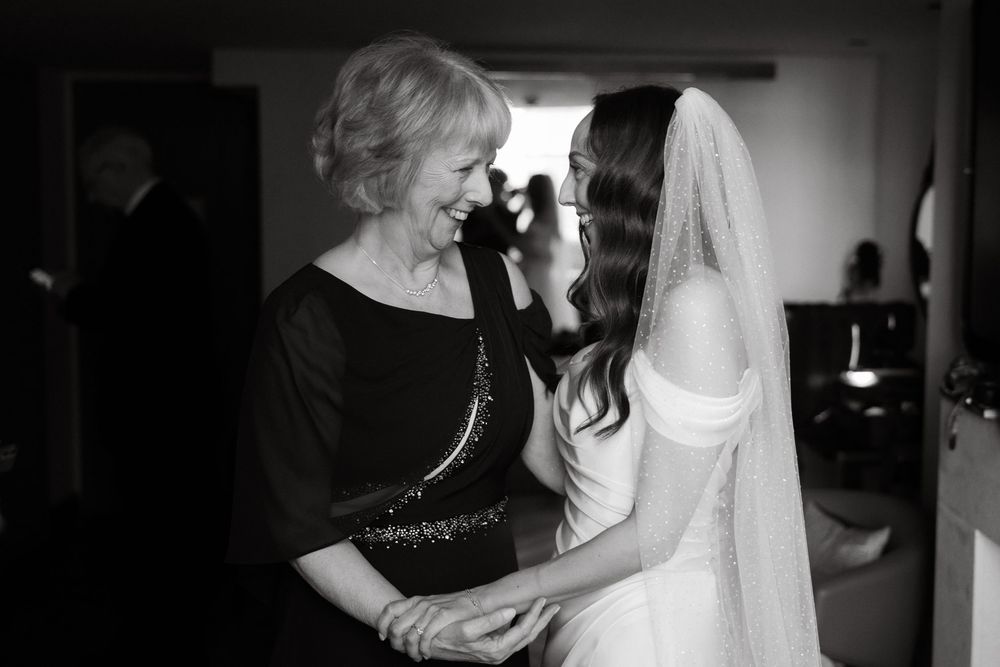 A tender black and white moment between a bride and woman in black during wedding preparations.