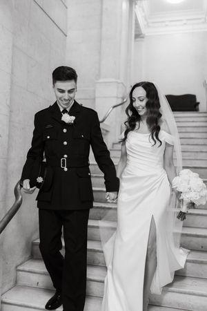 A couple in wedding attire descends marble stairs while holding hands, shown in a series of three black and white photos.