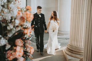 Bride and groom share romantic moments among elegant white columns and peach-colored floral decorations.
