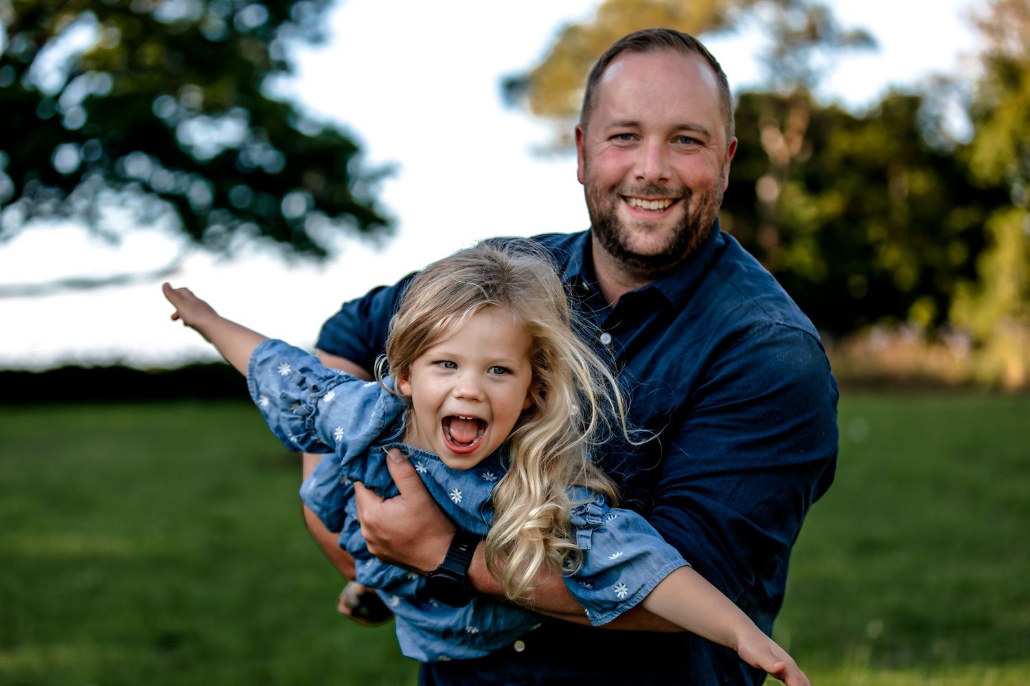Playful outdoor moment featuring joyful expressions and outstretched arms in natural sunlight, captured by a Palmerston North family photogr