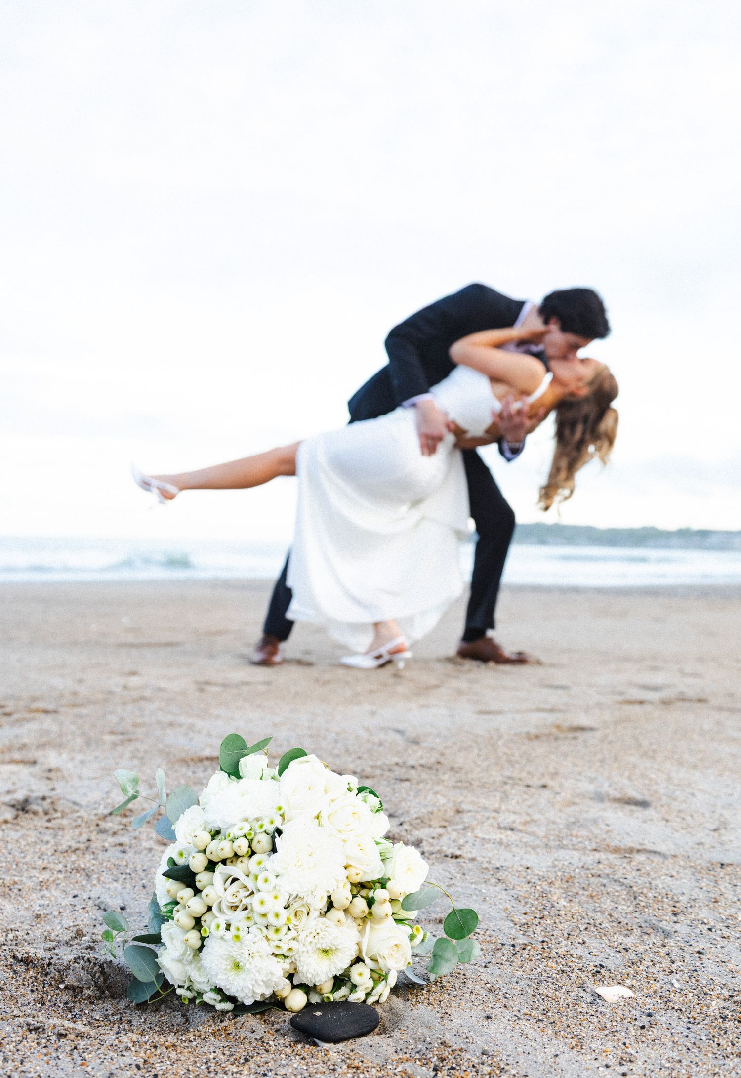 A romantic beach wedding photo sequence with a white floral bouquet in the foreground and a couple posing in the sand.