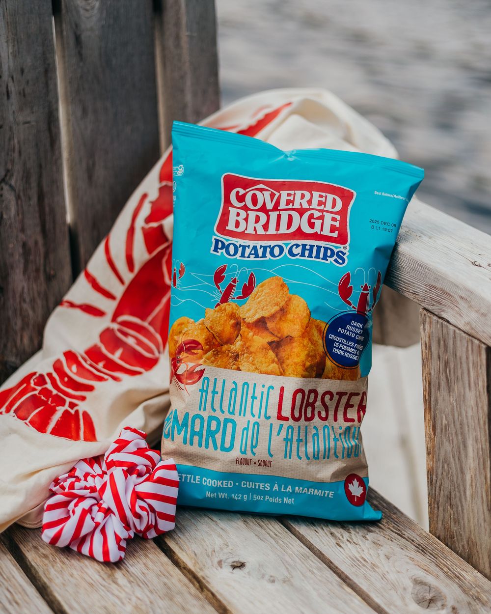 Several bags of Cape Cod branded potato chips in lobster flavors arranged with red and white decorative elements on wooden surface.
