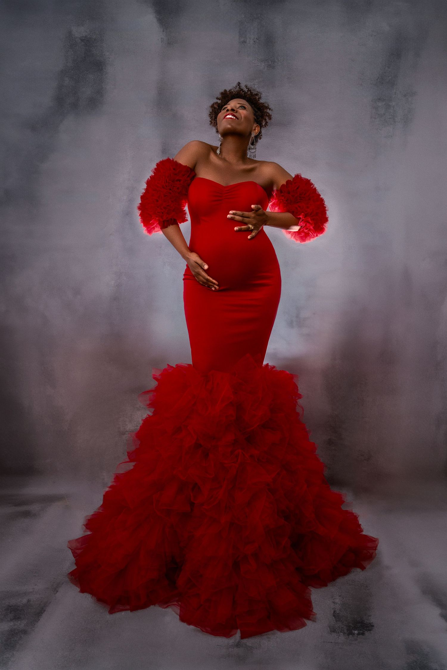 Dramatic maternity photo featuring red mermaid gown against smoky grey background.