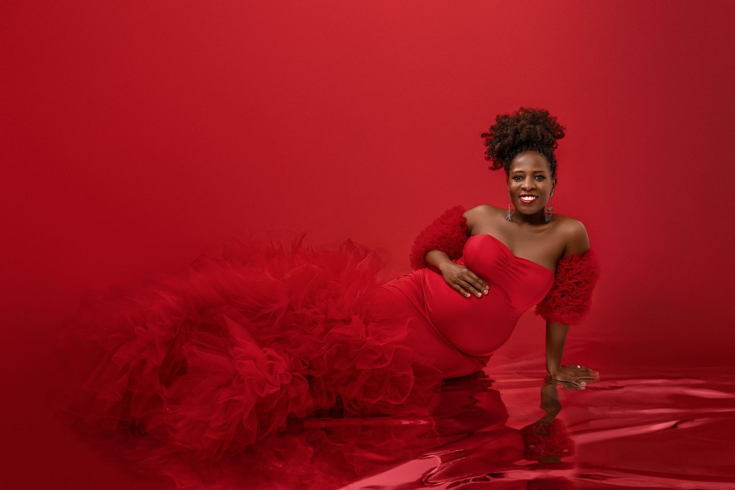 Maternity photo with flowing red dress against vibrant red background.