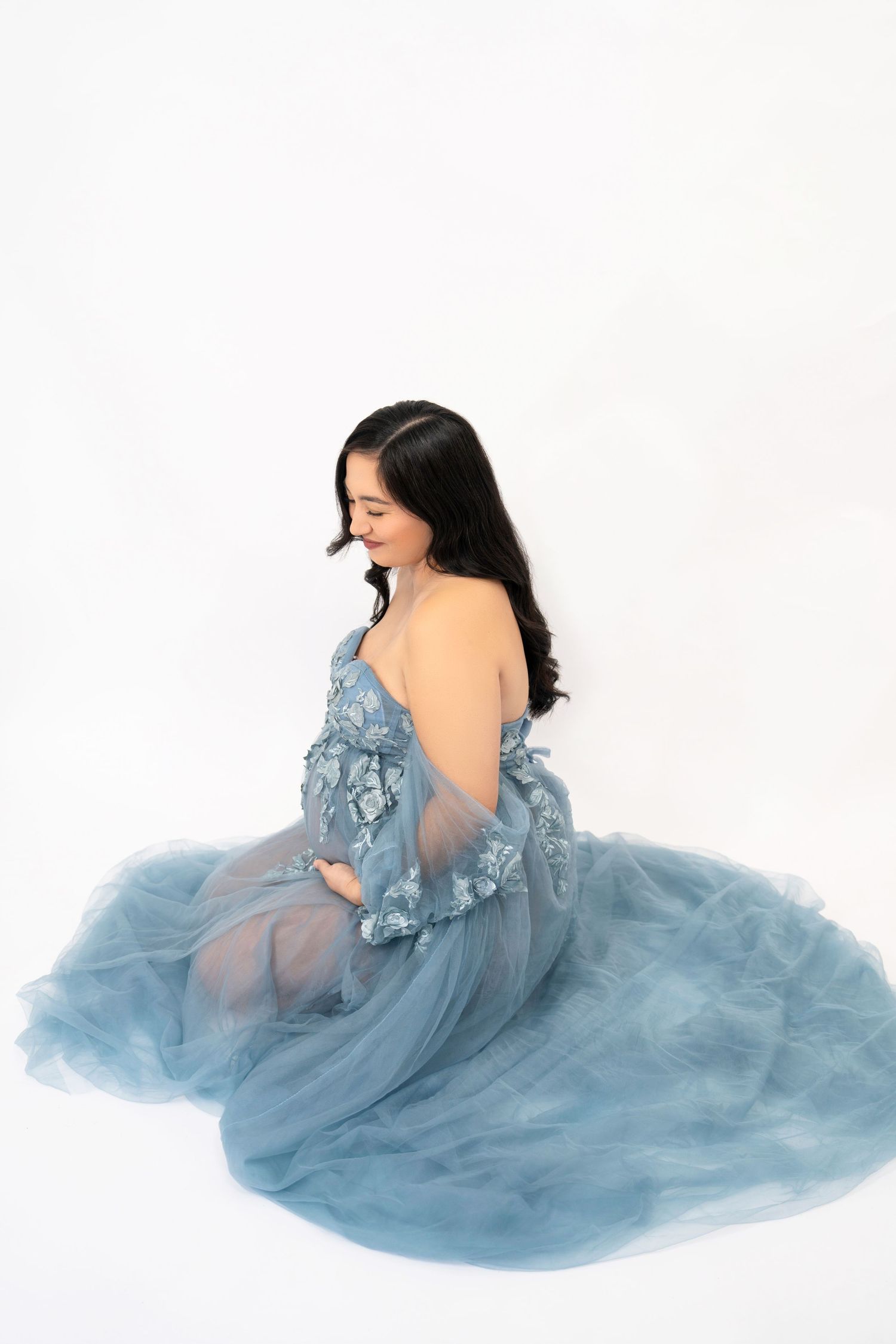 Side view maternity portrait in ethereal blue lace gown on white background.