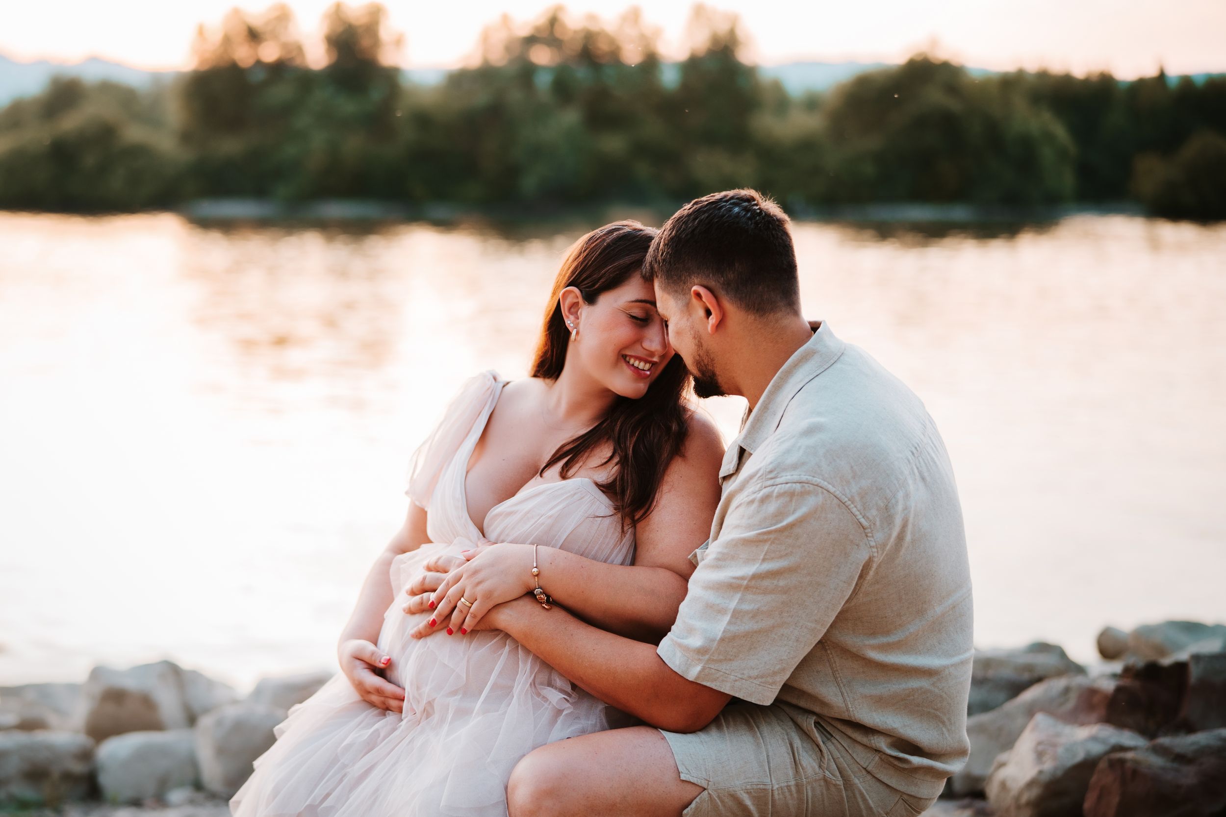 Romantic beach maternity photos at sunset with couple embracing on rocky shore.