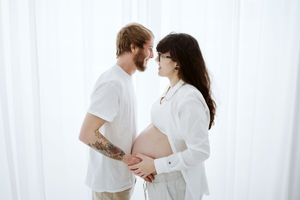 Minimalist maternity photoshoot featuring couple in white against bright backdrop.