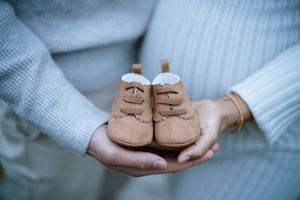 Close-up of tiny brown baby shoes held against soft blue knit background.