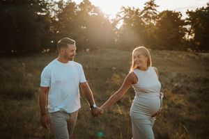 Couple holding hands during sunset maternity photo session in field.