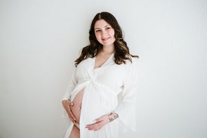Woman in white clothing against light background during maternity photoshoot.