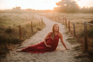 A flowing red dress contrasts beautifully against a misty beach path at golden hour.