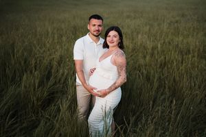 Romantic couple embracing in tall grass field during sunset maternity session.