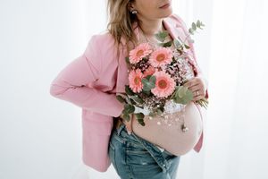 Woman in pink blazer holding fresh floral bouquet against white background.
