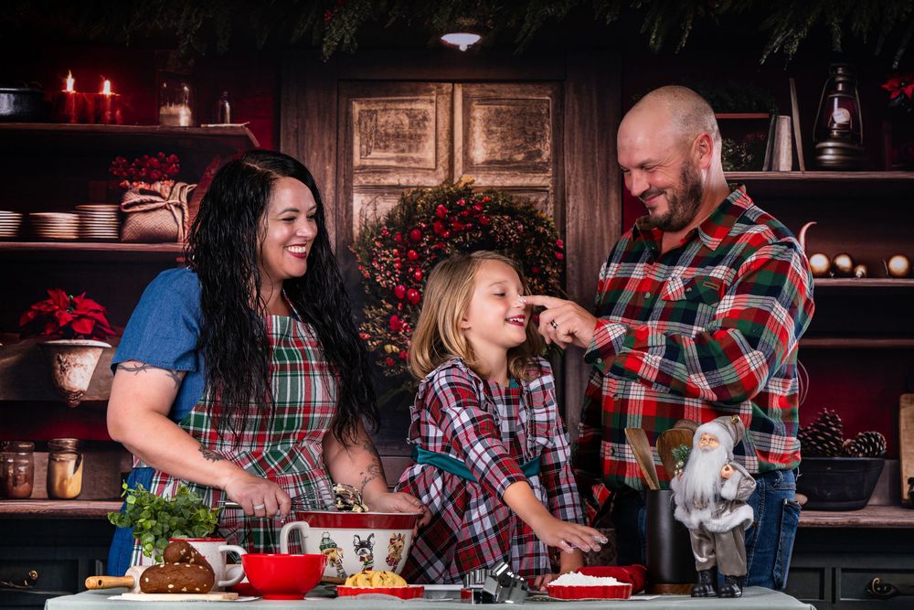 A family laughs while cooking together in their kitchen decorated for the holidays.