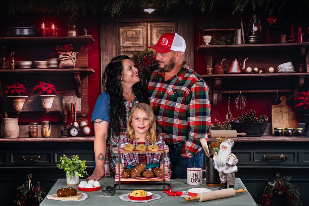A family stands together at a kitchen counter with holiday treats and decorations.