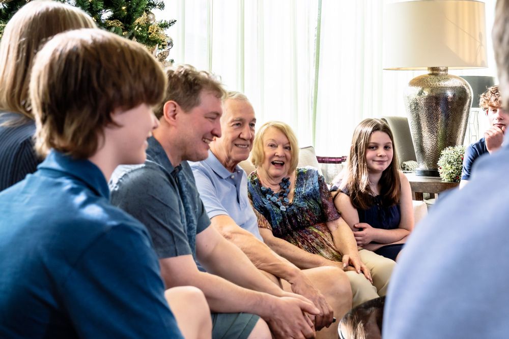 People gathered in festive room with Christmas decorations and natural lighting.
