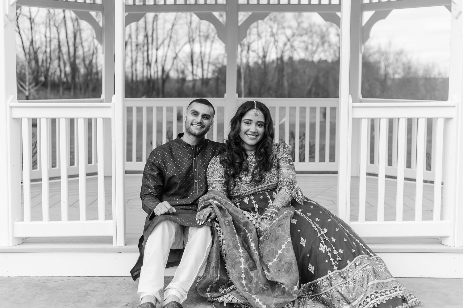Black and white photo of couple in traditional attire at a white gazebo.