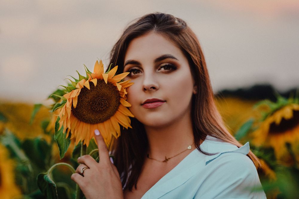 Fashion portrait in a sunflower field with dramatic lighting and soft colors.