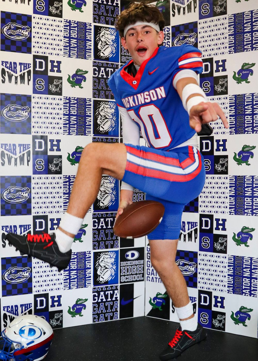 Football players pose in front of team backdrop wearing blue and red uniforms.