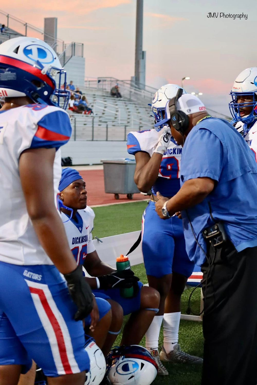 Football team members gather on the sidelines at sunset wearing blue and white uniforms.