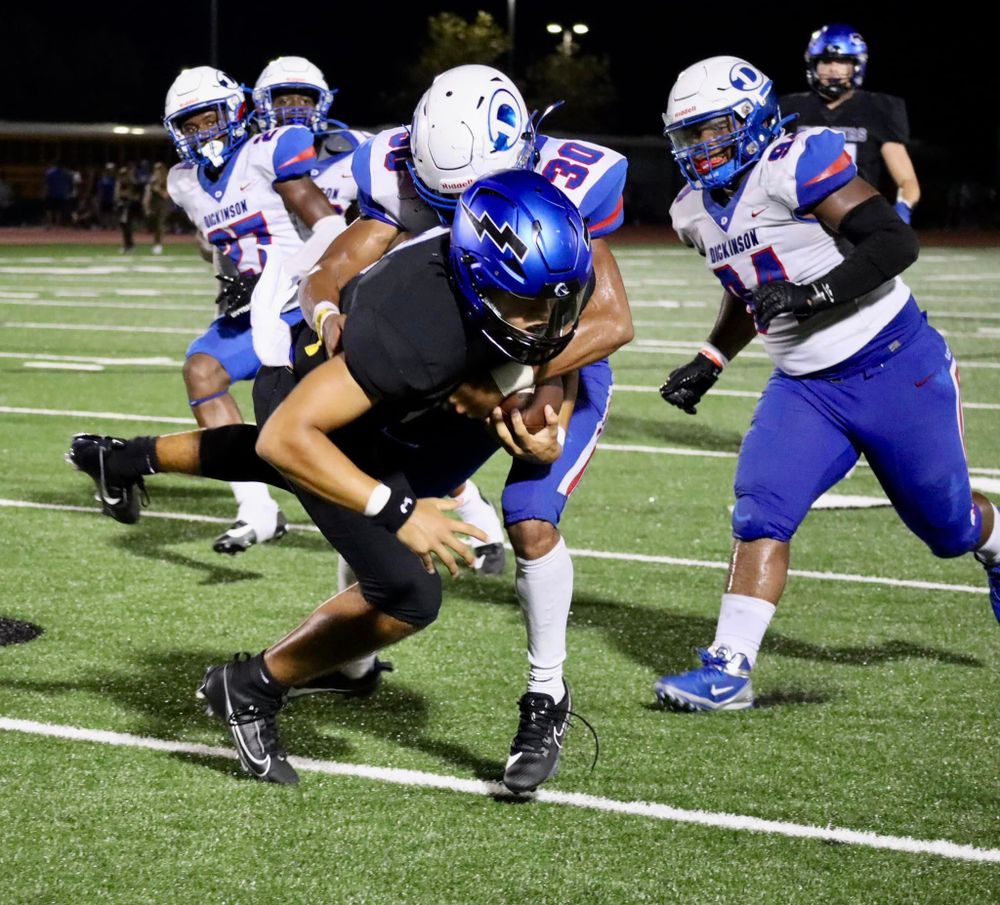 Football players engage in an intense ground play during a nighttime game.