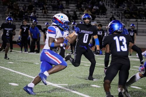 Football players in blue jerseys execute defensive drills during nighttime practice.