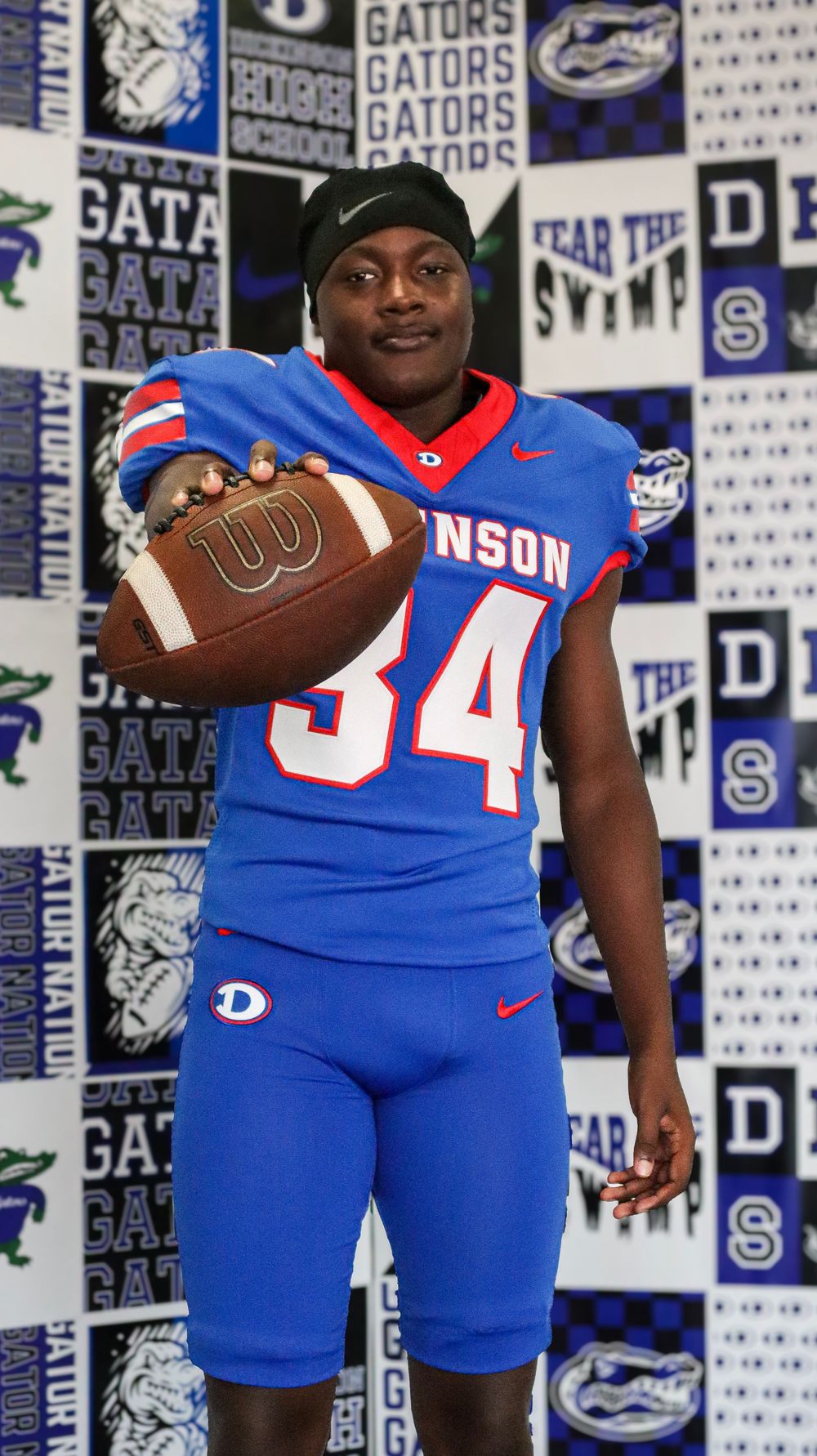 Florida Gators football players pose with footballs in blue uniforms against team-branded backdrop.