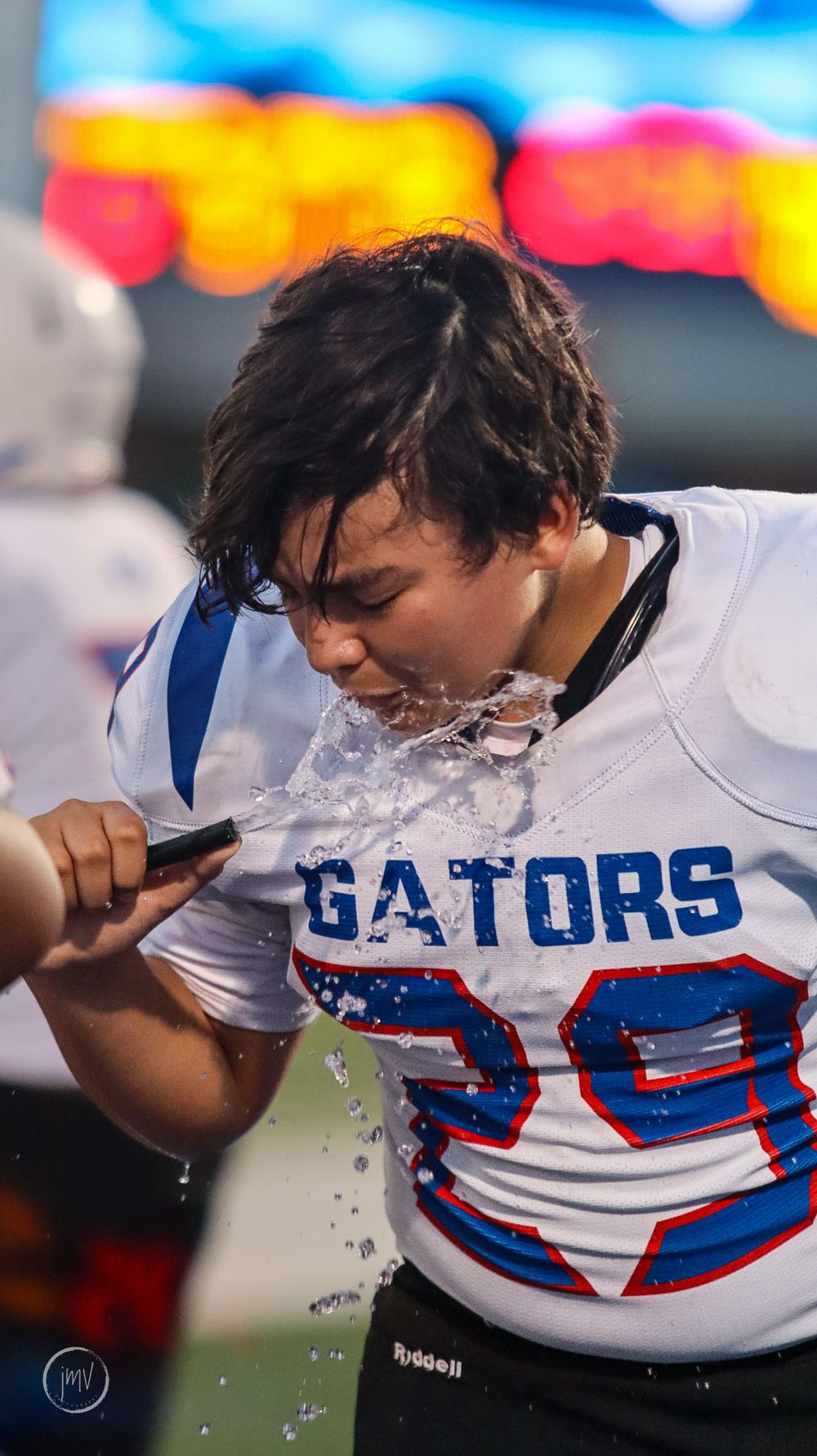 Football player splashes water on face to cool down during game.