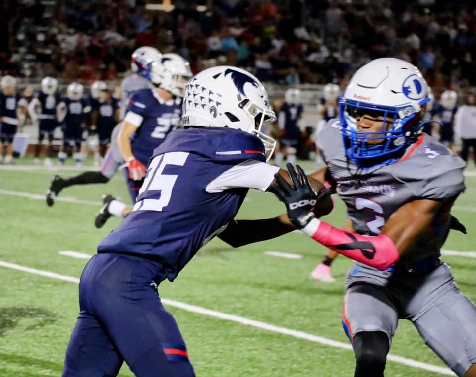 Football players from opposing teams engage in gameplay action on the field at night.