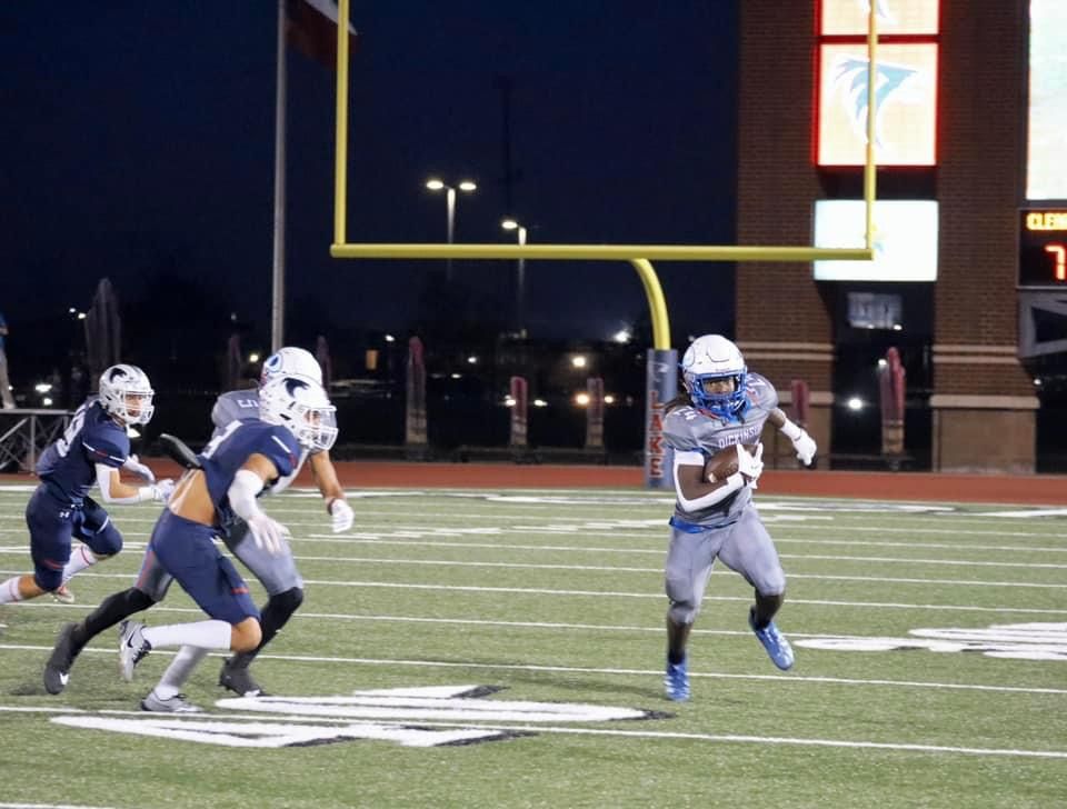 Football players in navy and gray uniforms compete during a nighttime game on the field.