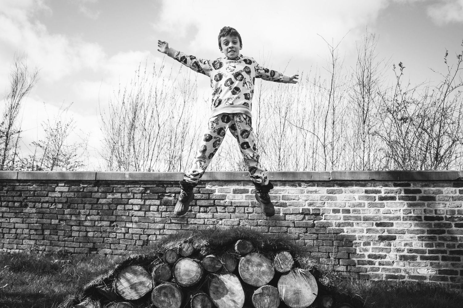 Black and white photograph of a person balanced atop a brick wall with logs below.