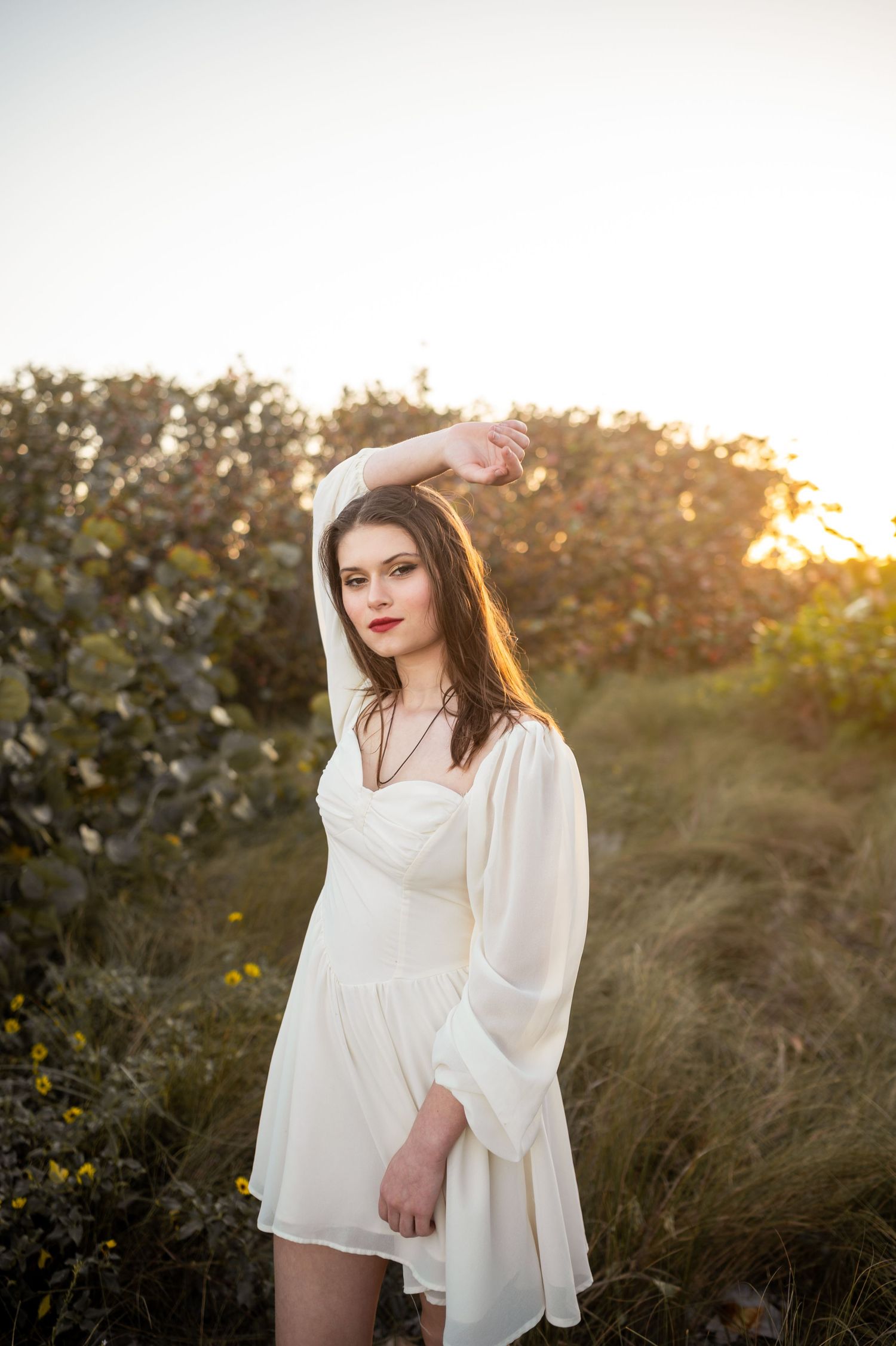 Senior girl graduation photoshoot session in white dress smiling standing in field park sunset Melbourne Cocoa Vero Florida Brevard County