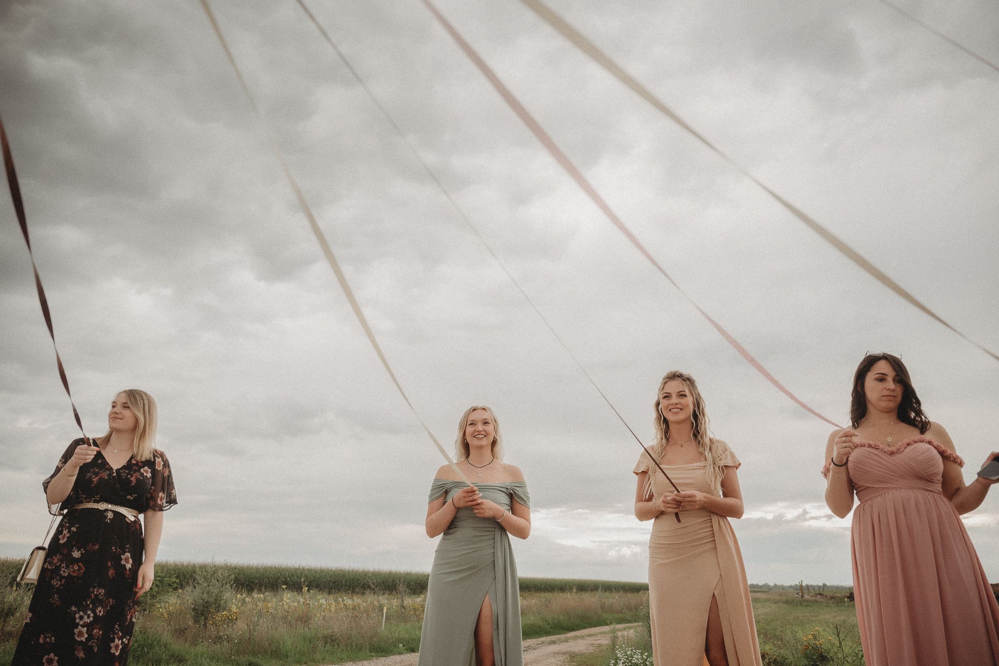 Four bridesmaids in pastel dresses standing against cloudy sky.