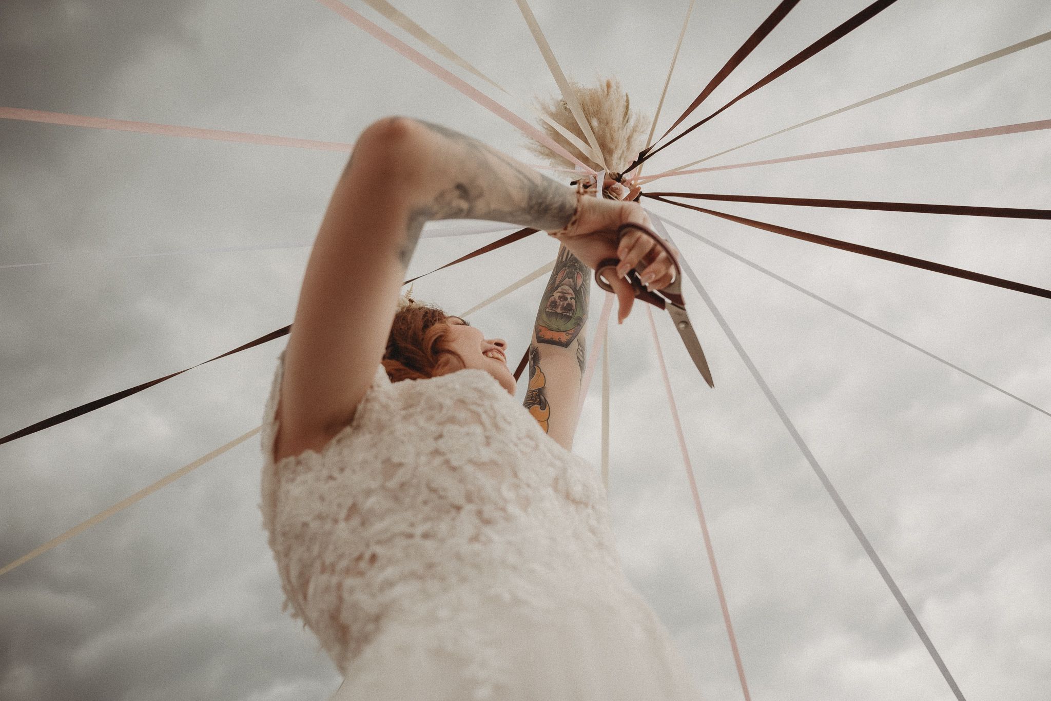 A person in a white lace wedding dress reaches up to grasp a decorative structure under moody skies.