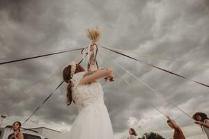 Person in flowing white dress reaches up to grab decorative elements against dramatic cloudy sky.