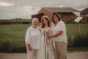 Three generations pose together on a rustic path with farmland in the background.