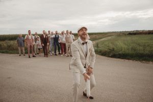 Wedding party follows behind someone in formal attire walking down rural pathway.
