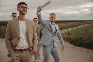 Wedding attendees in casual suits share a fun moment on a country road.